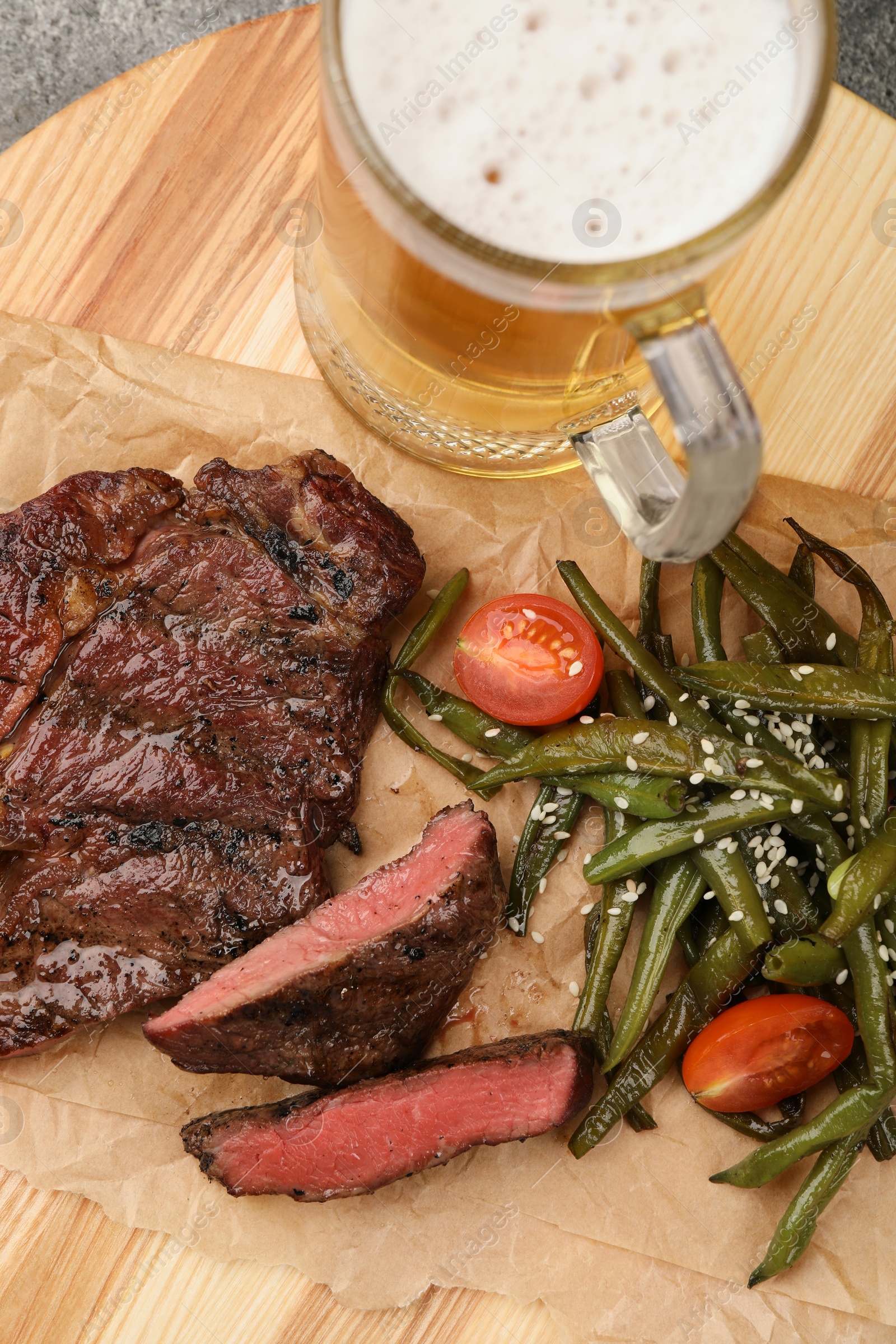 Photo of Mug with beer, delicious fried steak and asparagus on wooden table, above view