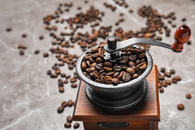 Coffee grinder with roasted beans on grey background