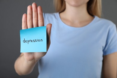 Photo of Woman showing sticky note with word Depression on grey background, closeup. Space for text