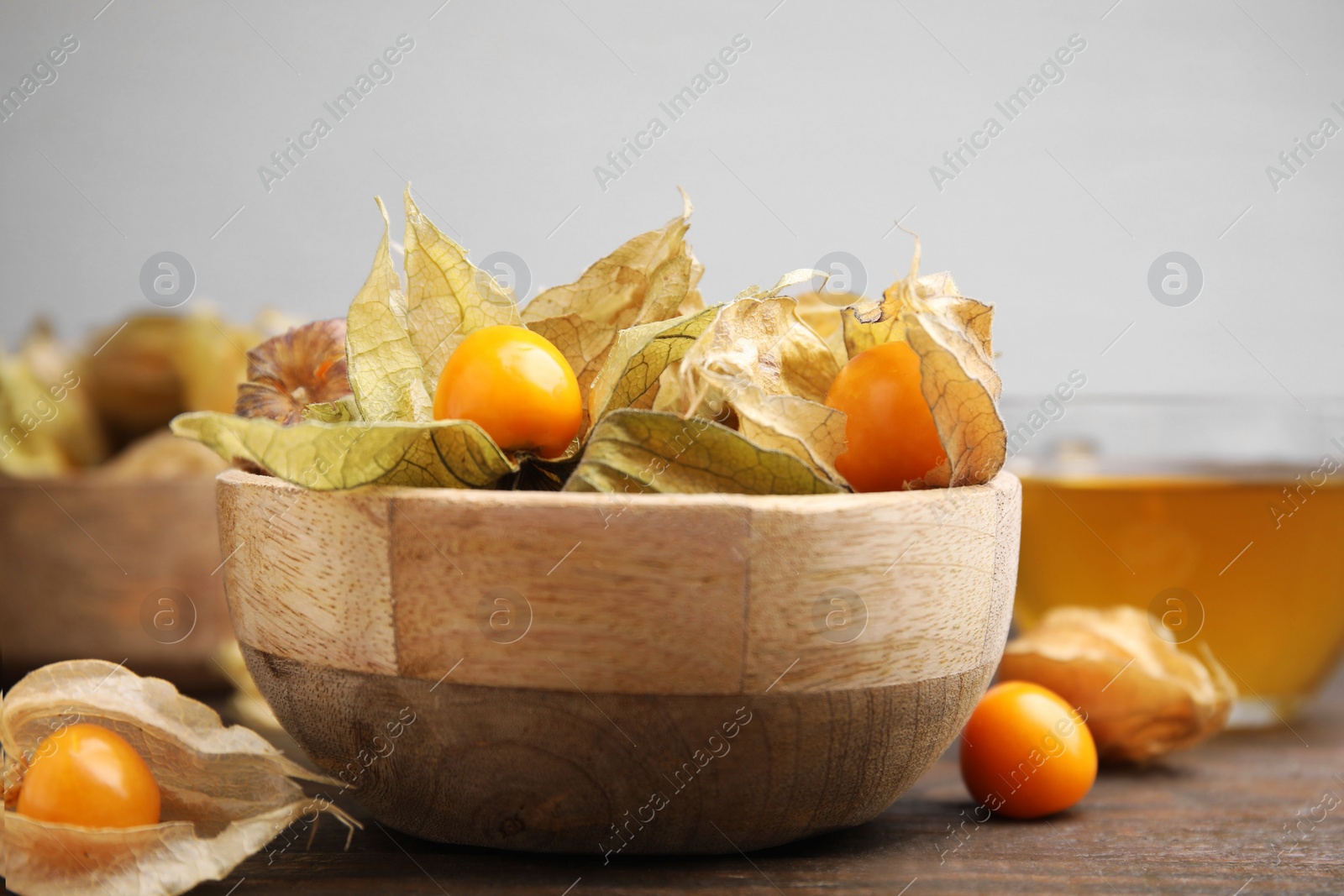 Photo of Ripe physalis fruits with calyxes in bowl on wooden table, closeup