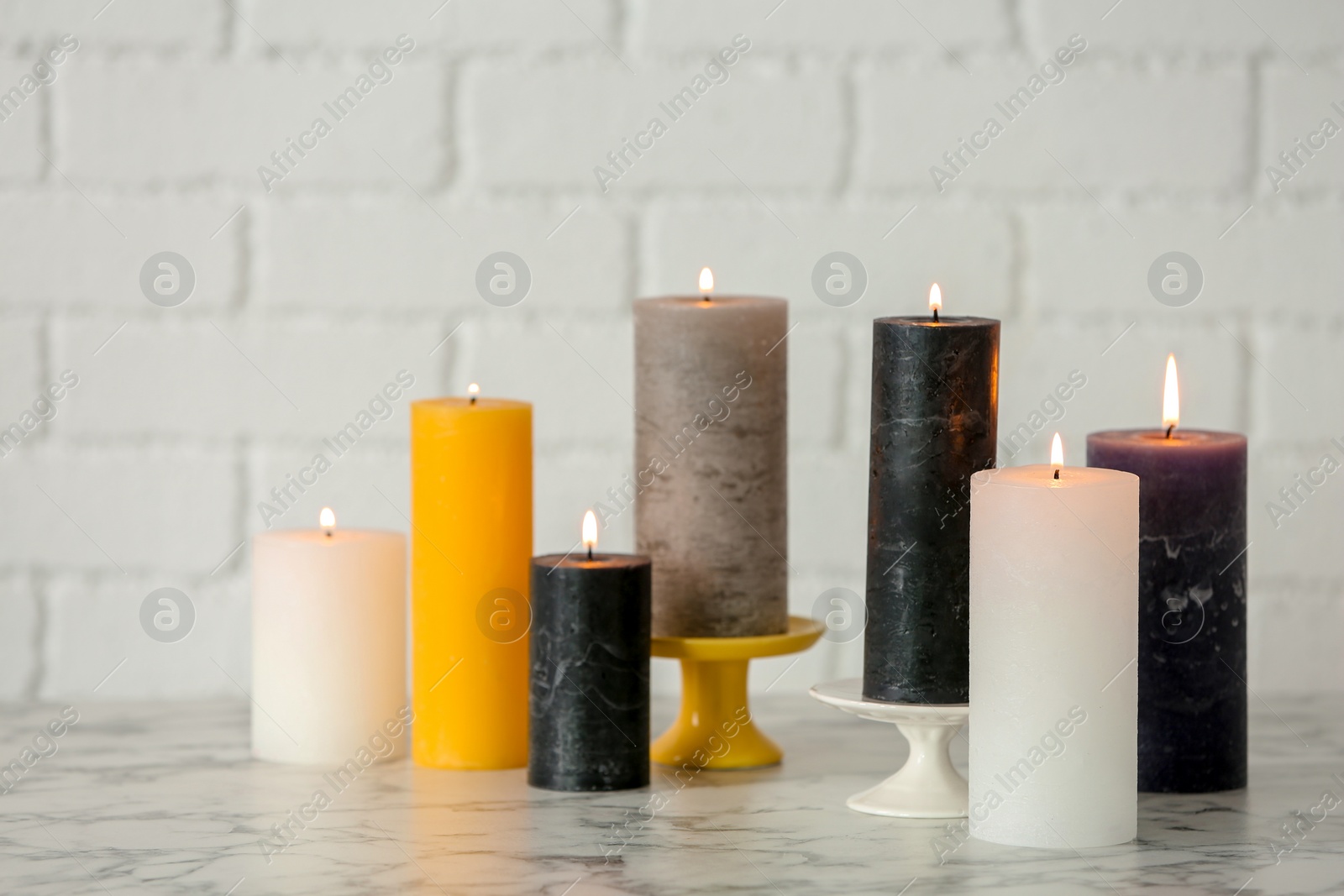 Photo of Different decorative wax candles on table against brick wall