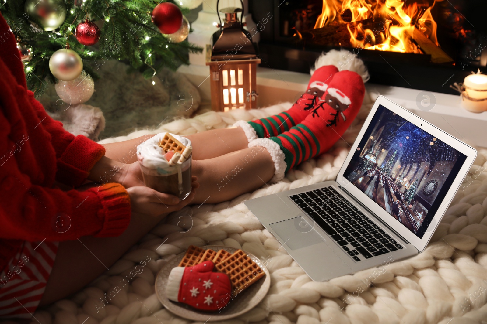 Photo of MYKOLAIV, UKRAINE - DECEMBER 23, 2020: Woman with sweet drink watching Harry Potter and Philosopher's Stone movie on laptop near fireplace at home, closeup. Cozy winter holidays atmosphere