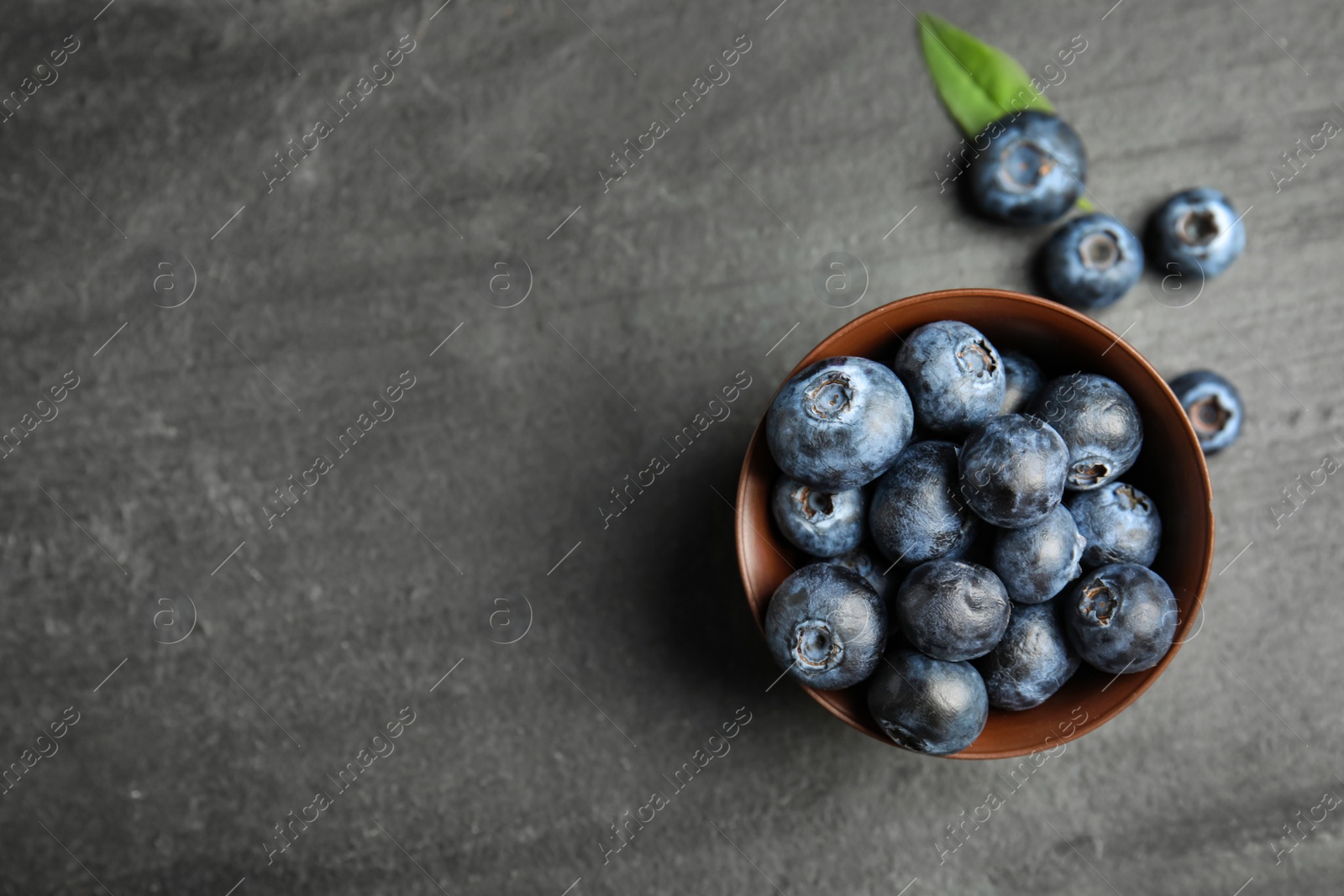 Photo of Fresh ripe blueberries in bowl on dark table, flat lay. Space for text