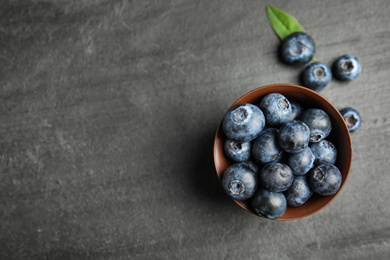 Photo of Fresh ripe blueberries in bowl on dark table, flat lay. Space for text