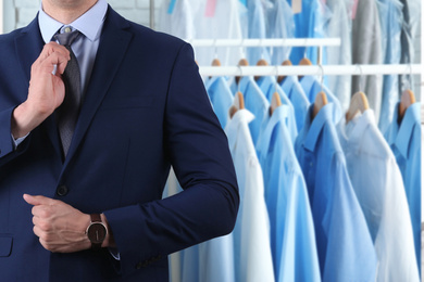 Businessman and rack with clean clothes at dry-cleaner's, closeup. Space for text 