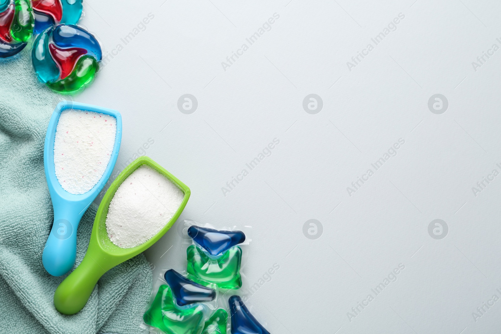 Photo of Laundry capsules, detergent powder and towel on light grey background, flat lay. Space for text