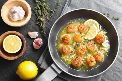 Photo of Delicious scallops with sauce in frying pan and ingredients on dark gray textured table, flat lay