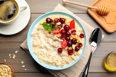 Photo of Bowl of oatmeal porridge served with berries on wooden table, flat lay