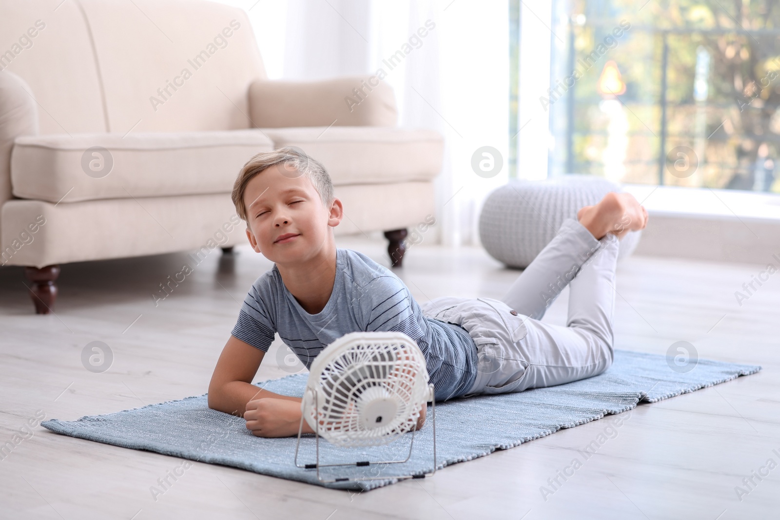 Photo of Little boy relaxing in front of fan at home. Summer heat