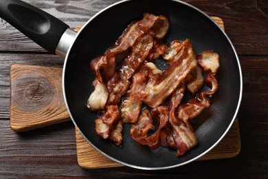 Delicious bacon slices in frying pan on wooden table, top view