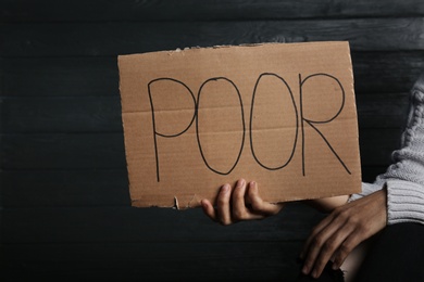 Woman holding cardboard sign with word "POOR" on wooden background, closeup