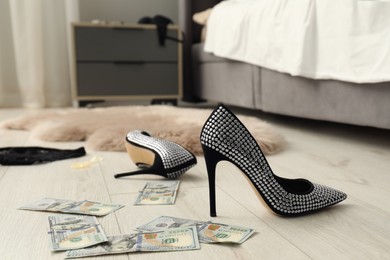Photo of Prostitution concept. High heeled shoes and dollar banknotes on floor indoors