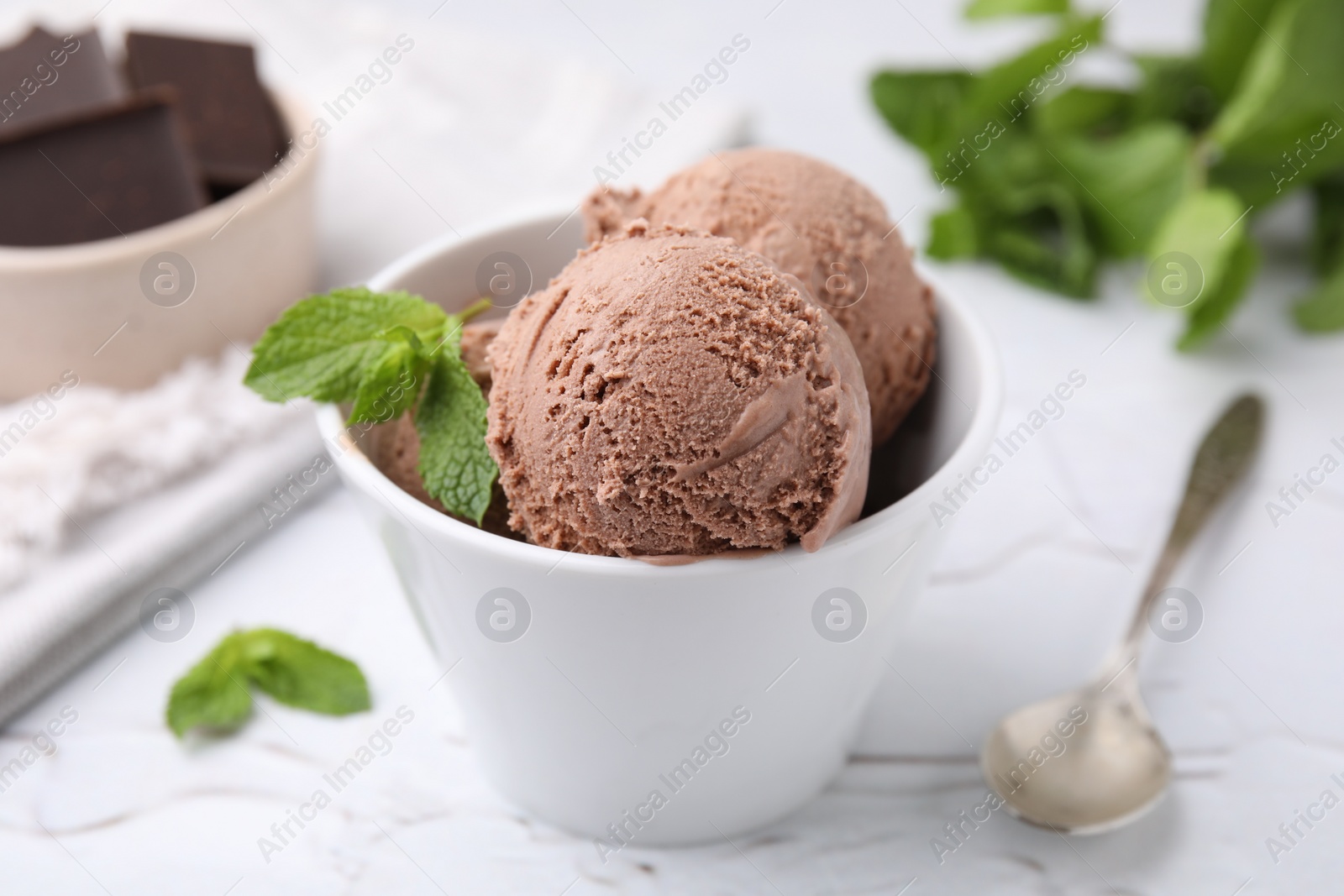 Photo of Bowl with tasty chocolate ice cream and mint leaves on white table, closeup