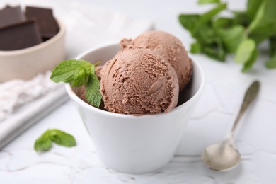 Bowl with tasty chocolate ice cream and mint leaves on white table, closeup