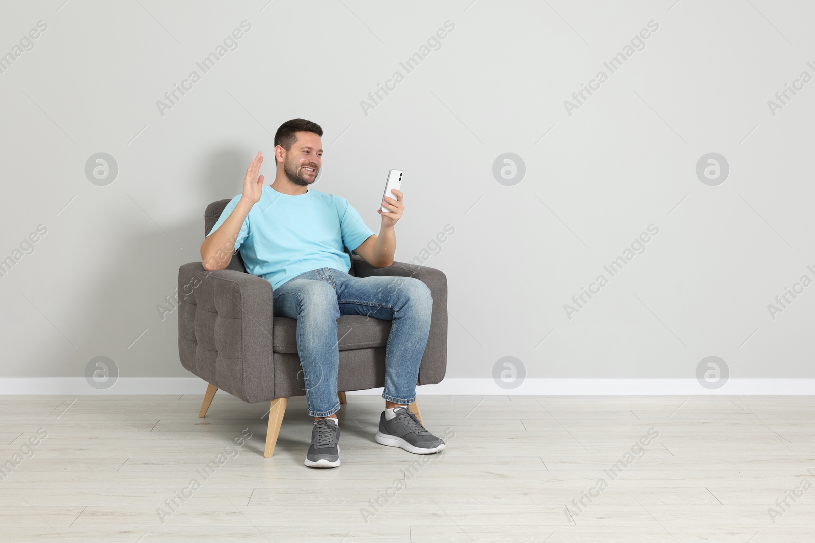 Photo of Happy man sitting in armchair and having video chat via smartphone indoors, space for text