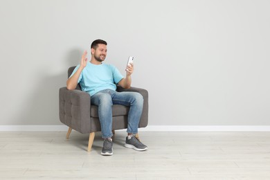 Happy man sitting in armchair and having video chat via smartphone indoors, space for text
