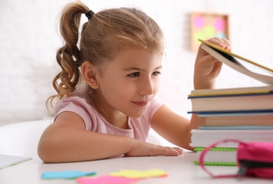 Photo of Cute little girl with books doing homework at table