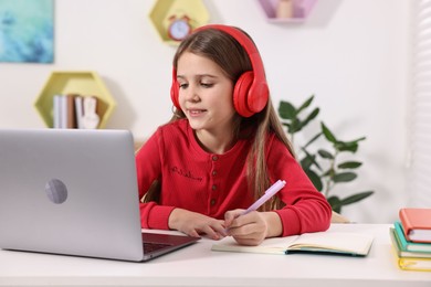 Photo of E-learning. Cute girl taking notes during online lesson at table indoors