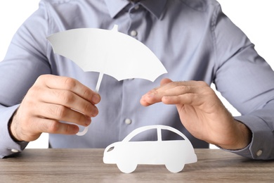 Male insurance agent covering paper car with umbrella cutout and hand at table, closeup