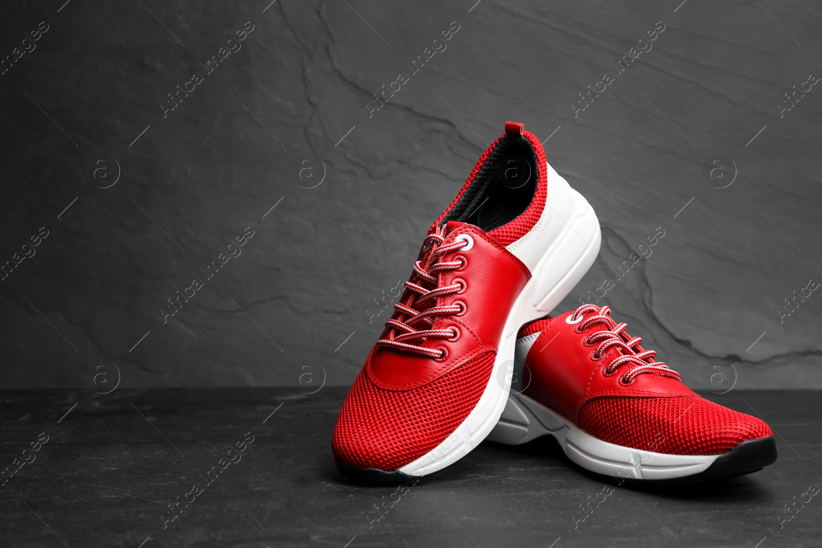Photo of Stylish red sneakers on black stone table. Space for text