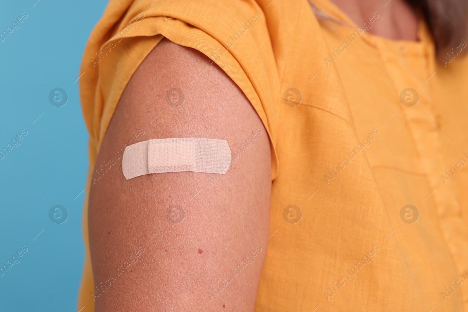 Photo of Woman with adhesive bandage on her arm after vaccination against light blue background, closeup