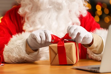 Photo of Santa Claus decorating Christmas gift with ribbon at home, closeup