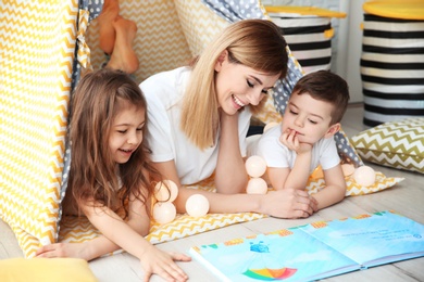 Photo of Nanny and little children reading book in tent at home