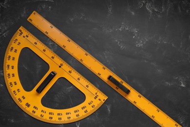Photo of Ruler and protractor with measuring length and degree markings on blackboard, flat lay. Space for text