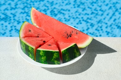 Photo of Slices of watermelon on white plate near swimming pool outdoors