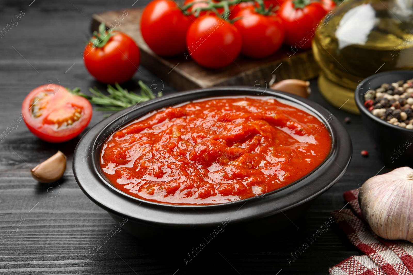 Photo of Homemade tomato sauce in bowl on black wooden table, closeup