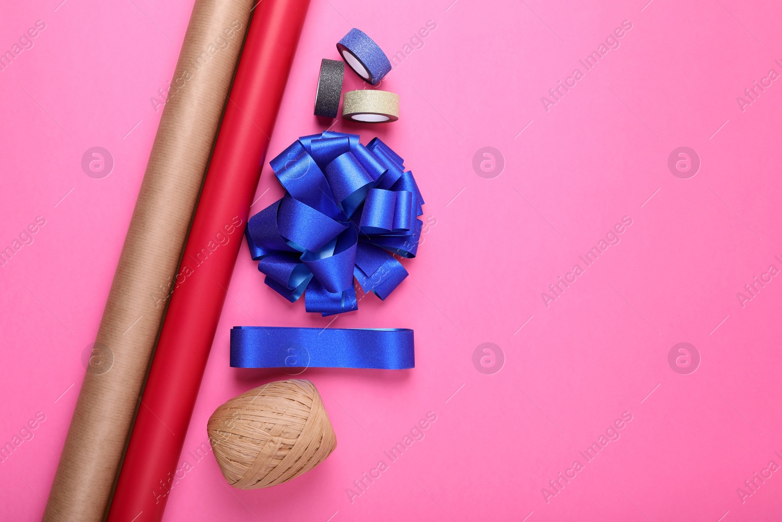 Photo of Rolls of wrapping paper, bow and ribbons on pink background, flat lay