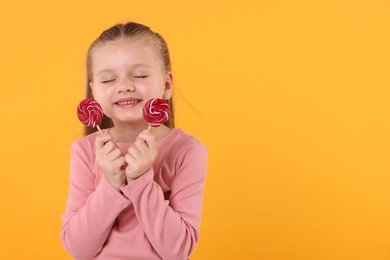 Happy little girl with bright lollipops on orange background, space for text