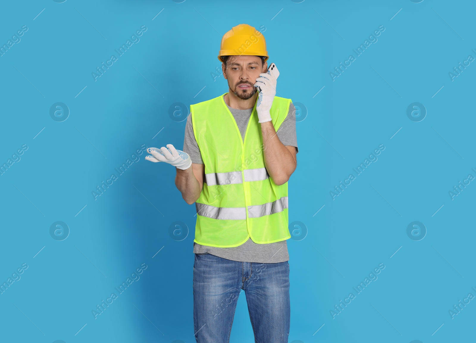 Photo of Male industrial engineer in uniform talking on phone against light blue background