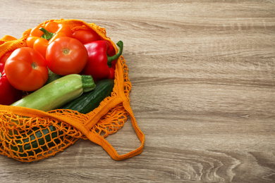 Photo of Net bag with vegetables on wooden table. Space for text