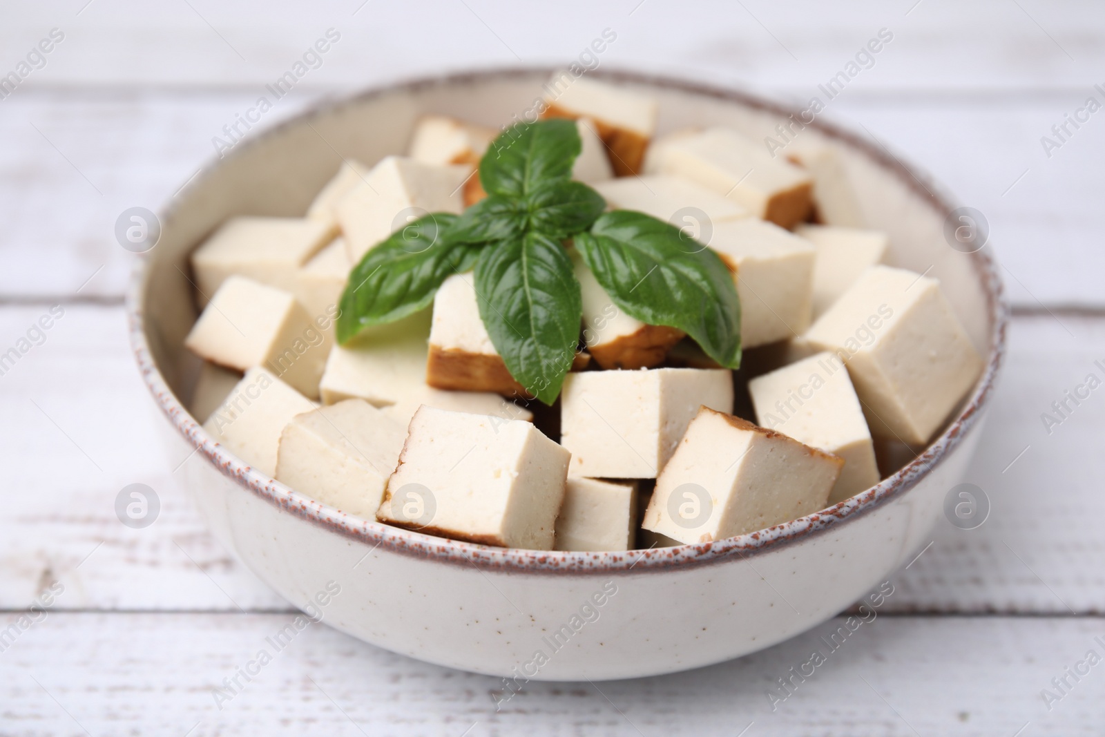 Photo of Bowl with delicious fried tofu and basil on white wooden table, closeup