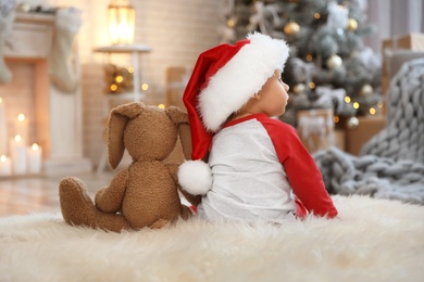 Photo of Little baby with Santa hat and toy on floor at home. First Christmas