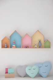 Photo of Colorful house shaped shelves on white wall and soft pillows indoors. Children's room interior design