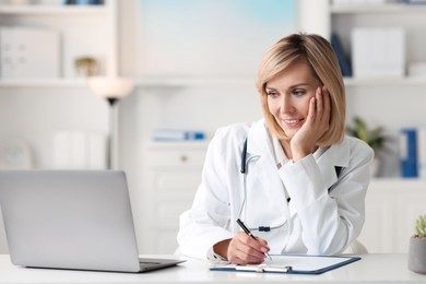 Photo of Smiling doctor with laptop having online consultation at table in office