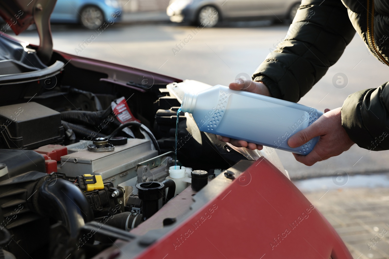 Photo of Man filling car radiator with antifreeze outdoors, closeup