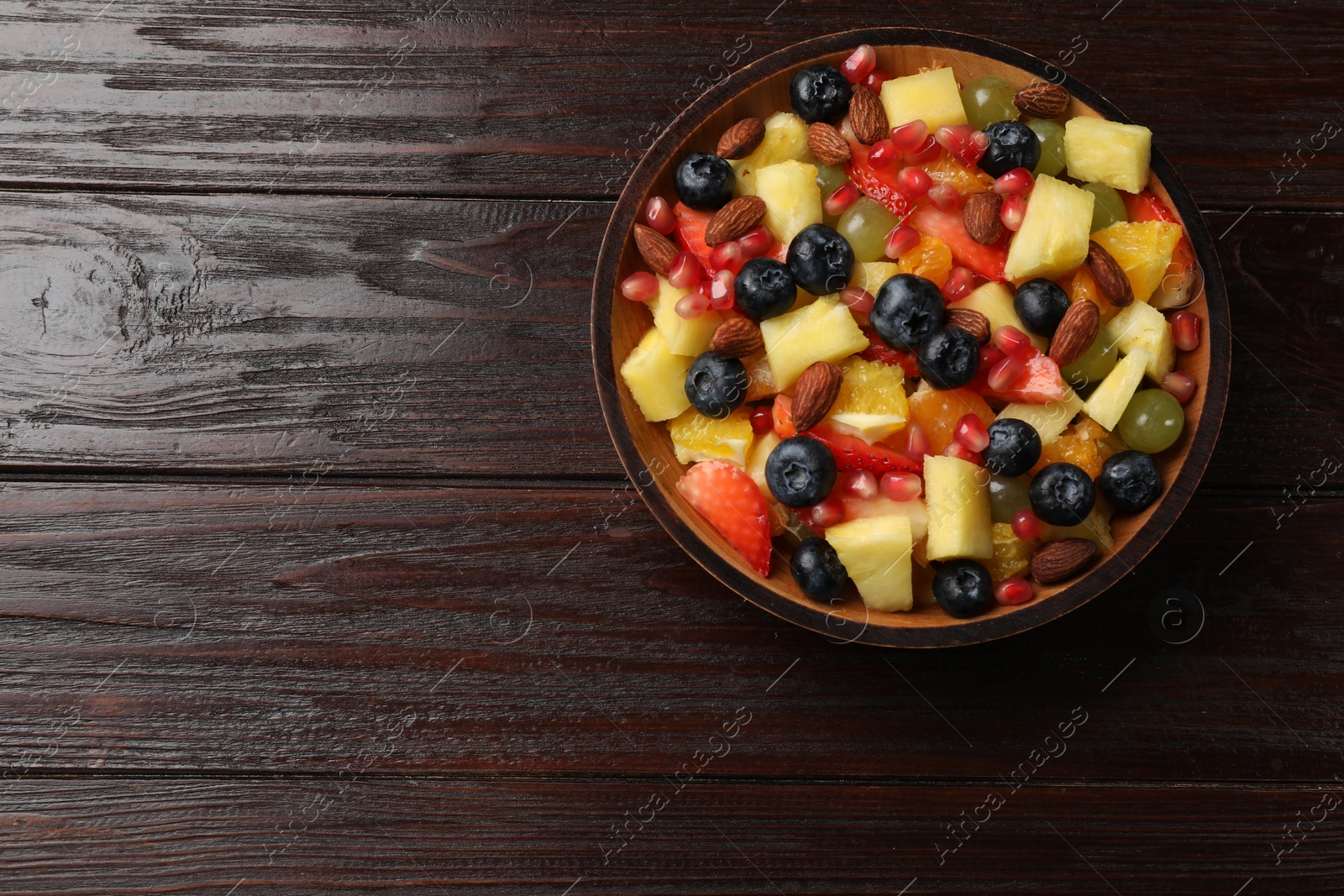 Photo of Delicious fruit salad in bowl on wooden table, top view. Space for text