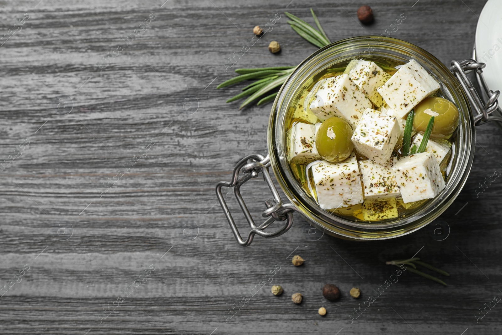 Photo of Pickled feta cheese in jar on grey wooden table, top view. Space for text