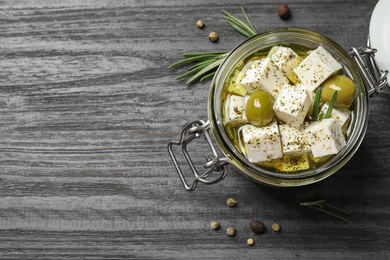 Photo of Pickled feta cheese in jar on grey wooden table, top view. Space for text