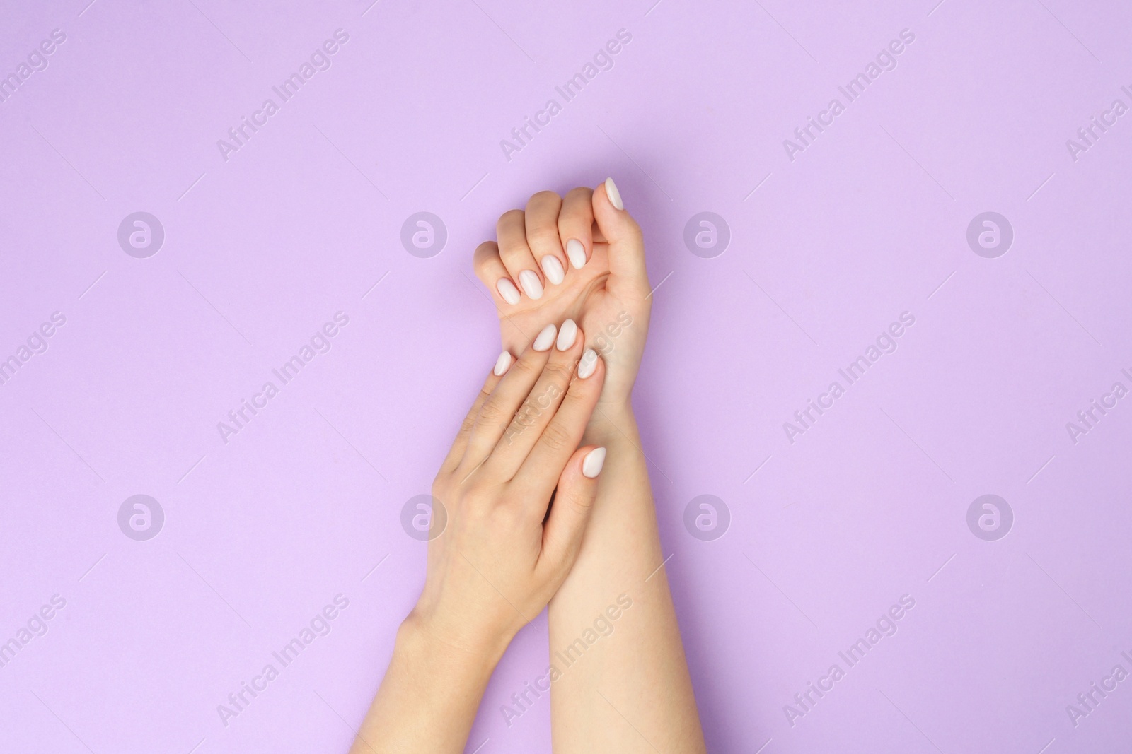 Photo of Woman with white polish on nails against violet background, top view