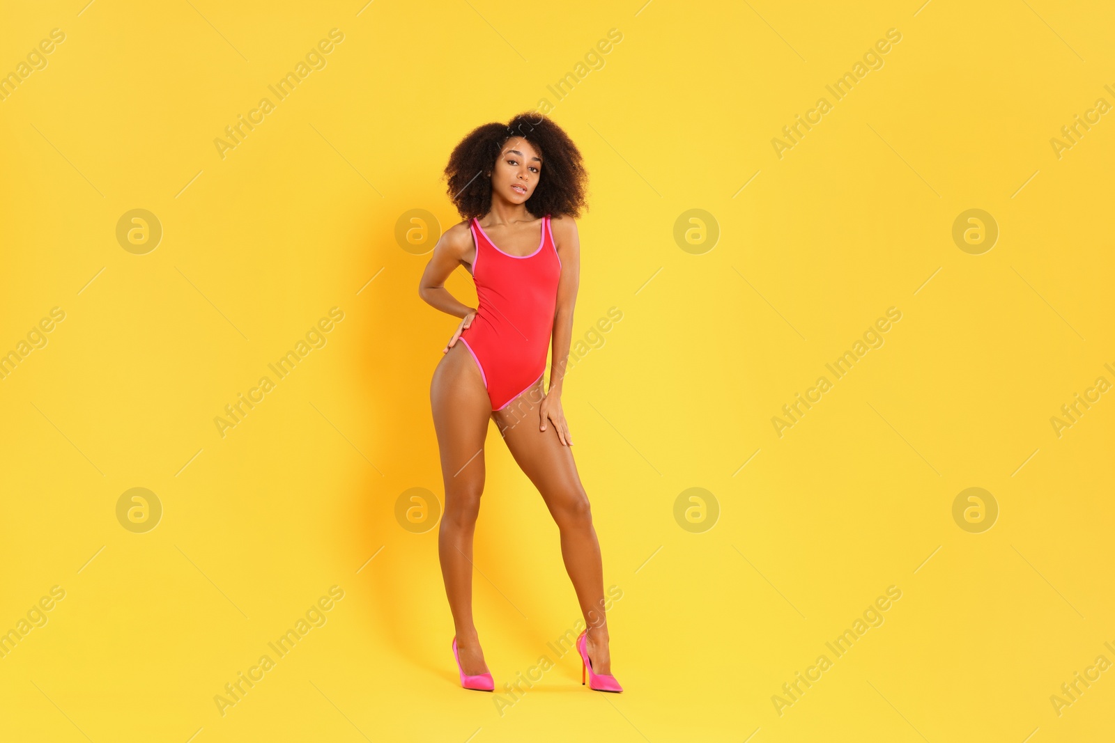 Photo of Beautiful woman in bright one-piece summer swimsuit and stylish high heel shoes on yellow background