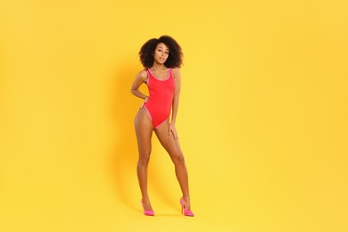 Photo of Beautiful woman in bright one-piece summer swimsuit and stylish high heel shoes on yellow background