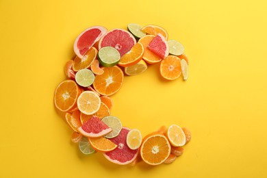 Photo of Letter C made with citrus fruits on yellow background as vitamin representation, flat lay