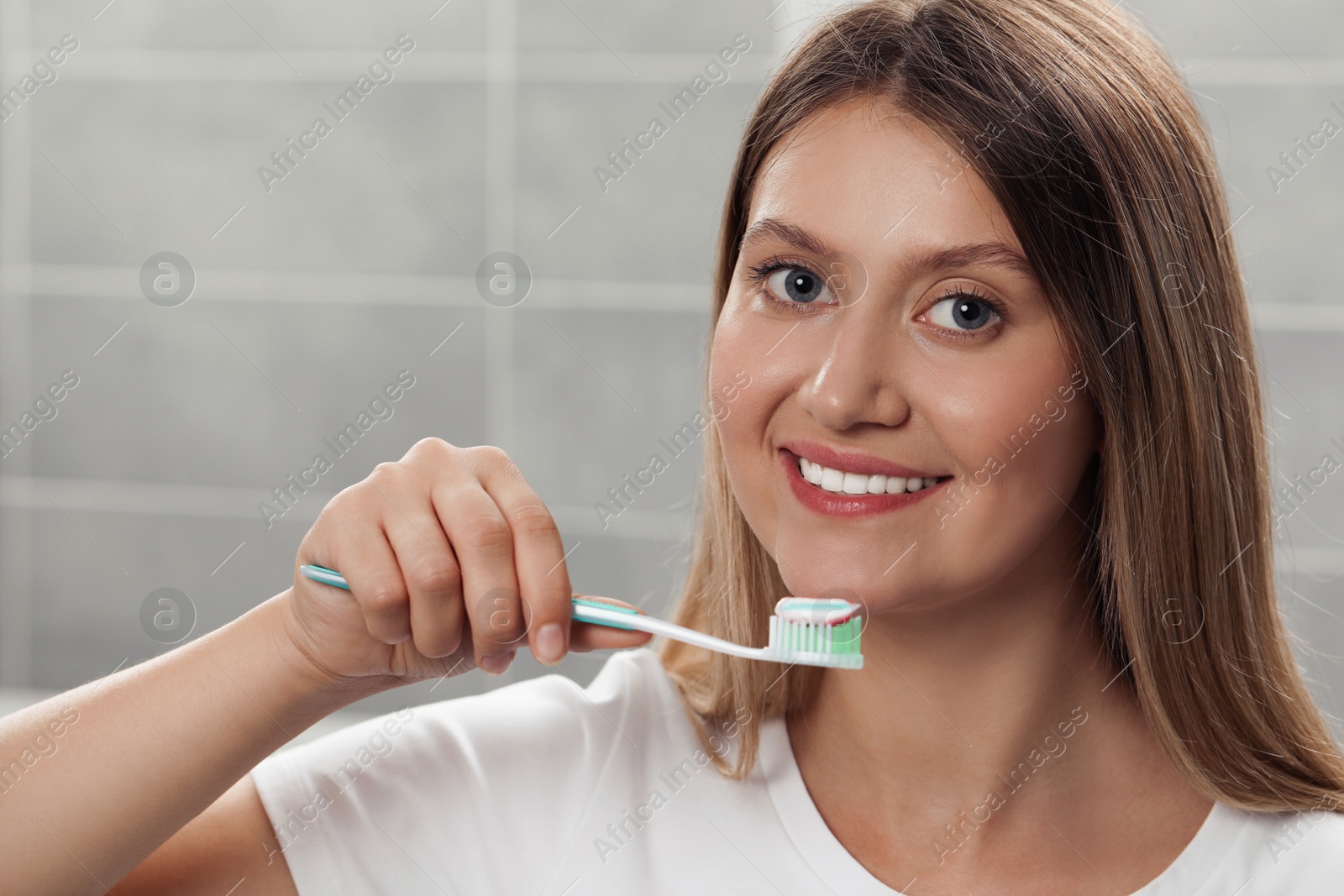 Photo of Young woman holding brush with toothpaste in bathroom