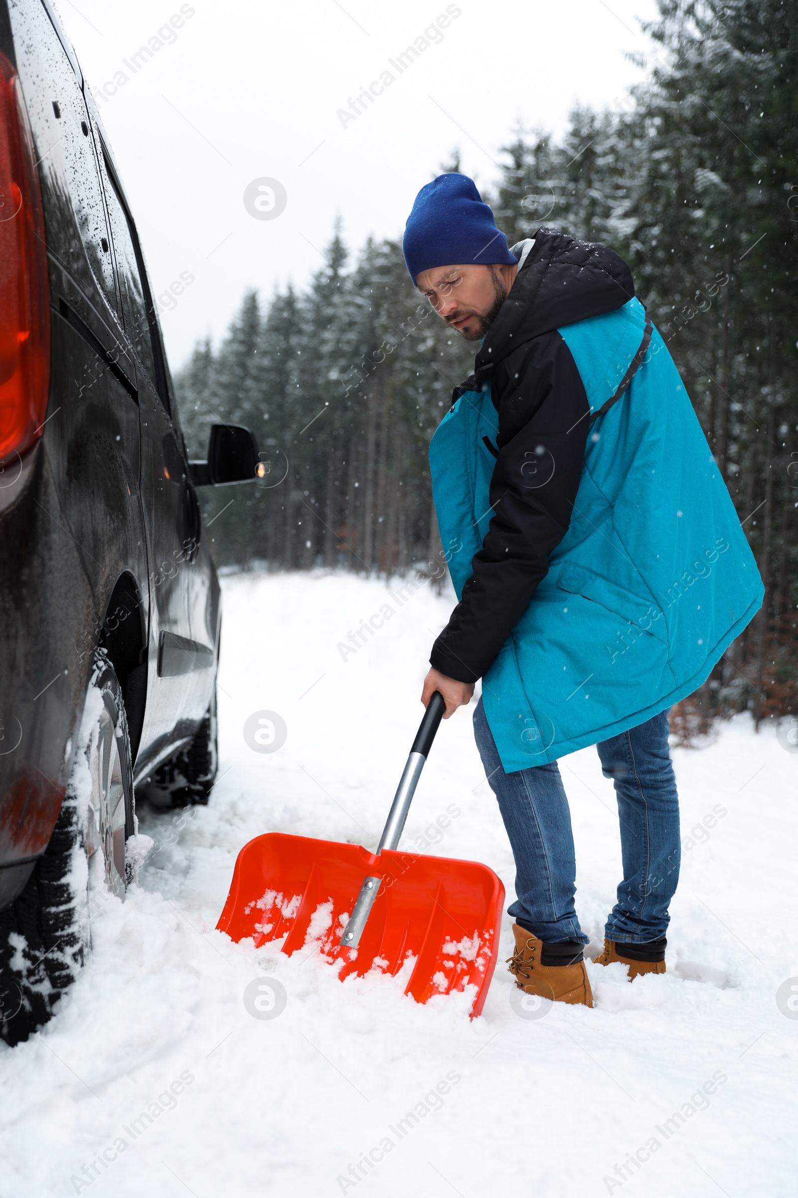 Photo of Man cleaning snow with shovel near stuck car outdoors