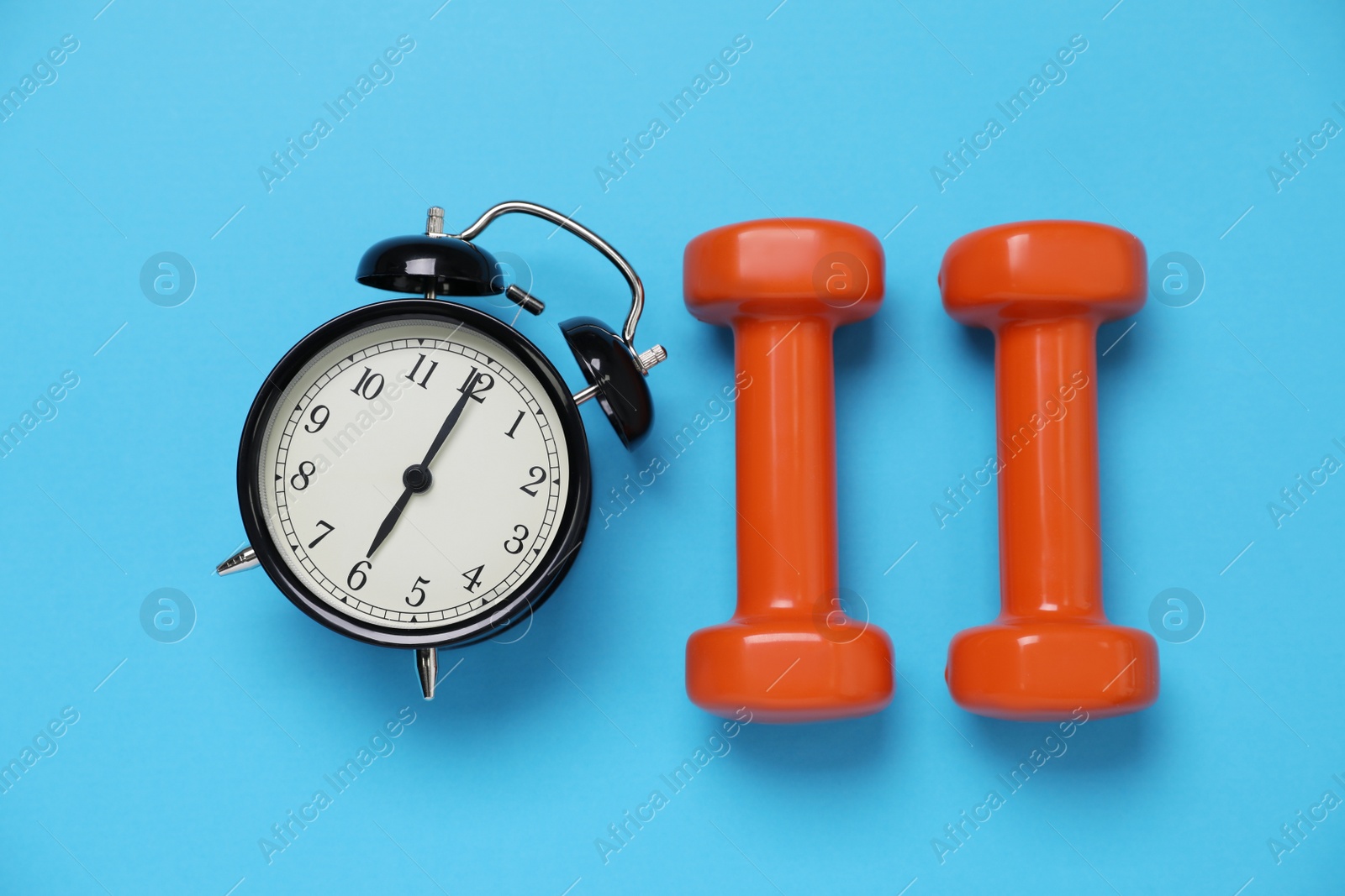 Photo of Alarm clock and dumbbells on light blue background, flat lay. Morning exercise