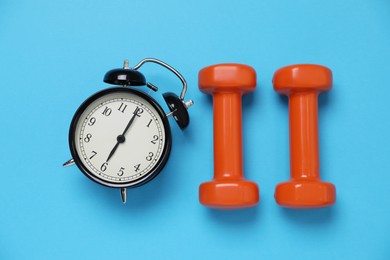 Alarm clock and dumbbells on light blue background, flat lay. Morning exercise